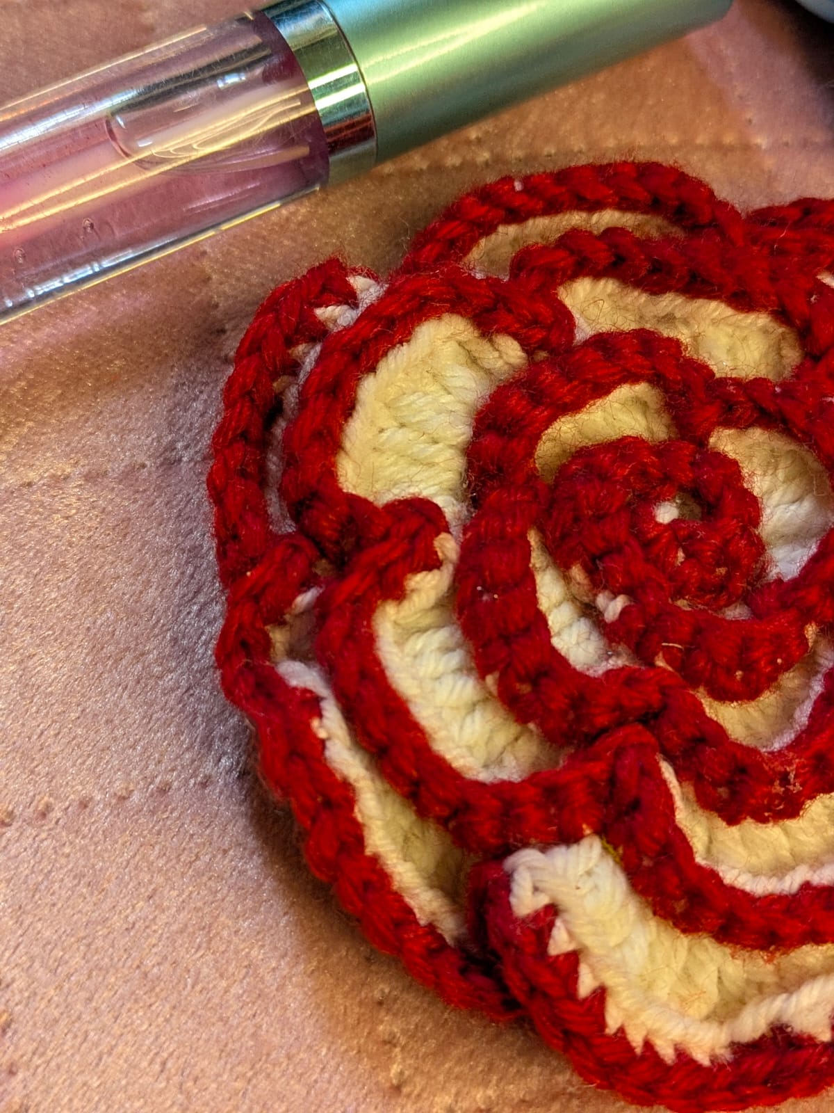 Red and cream handmade crochet piece photographed beside a lip gloss tube