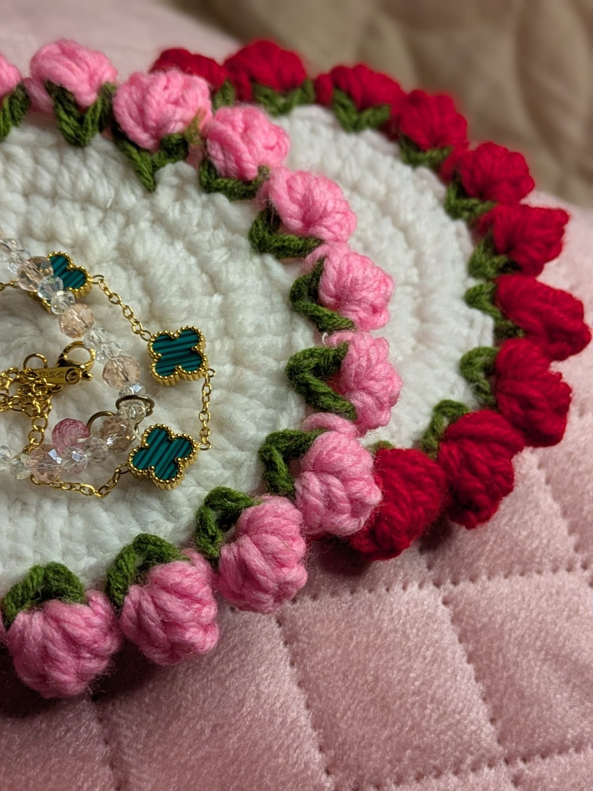 Pink and red crochet floral-edged piece photographed with a gold clover bracelet