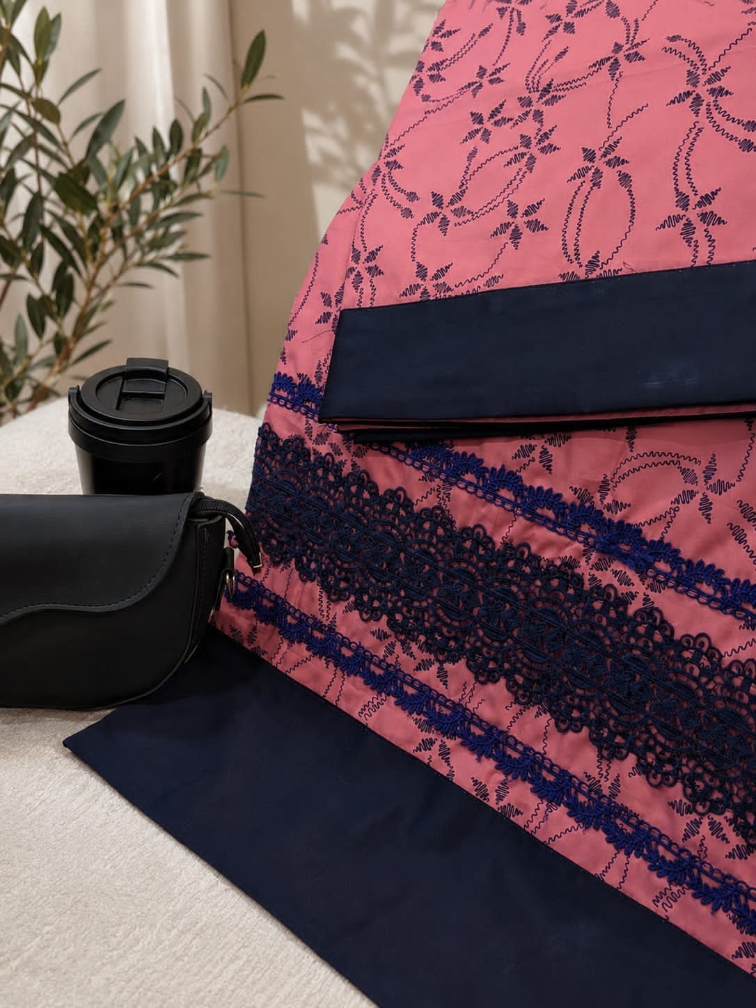 Pink textile with navy embroidery and lace trim styled with a black coffee cup and leather bag