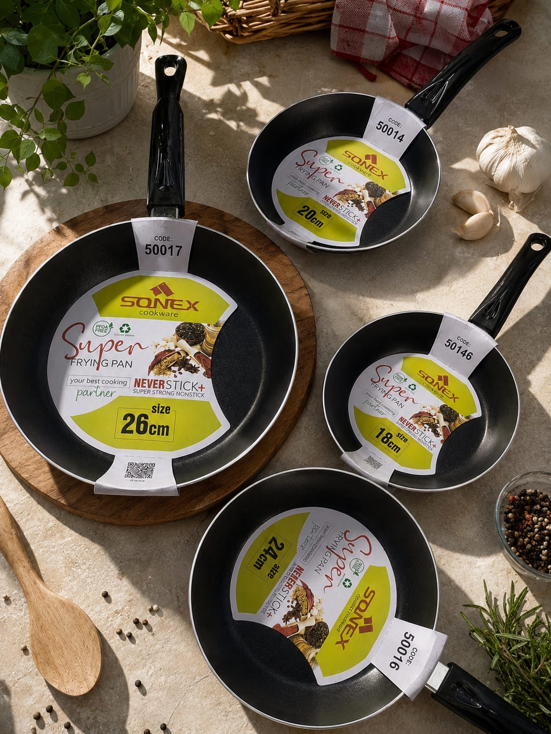 Four Sonex Super non-stick frying pans in different sizes arranged with garlic, herbs and a wooden spoon
