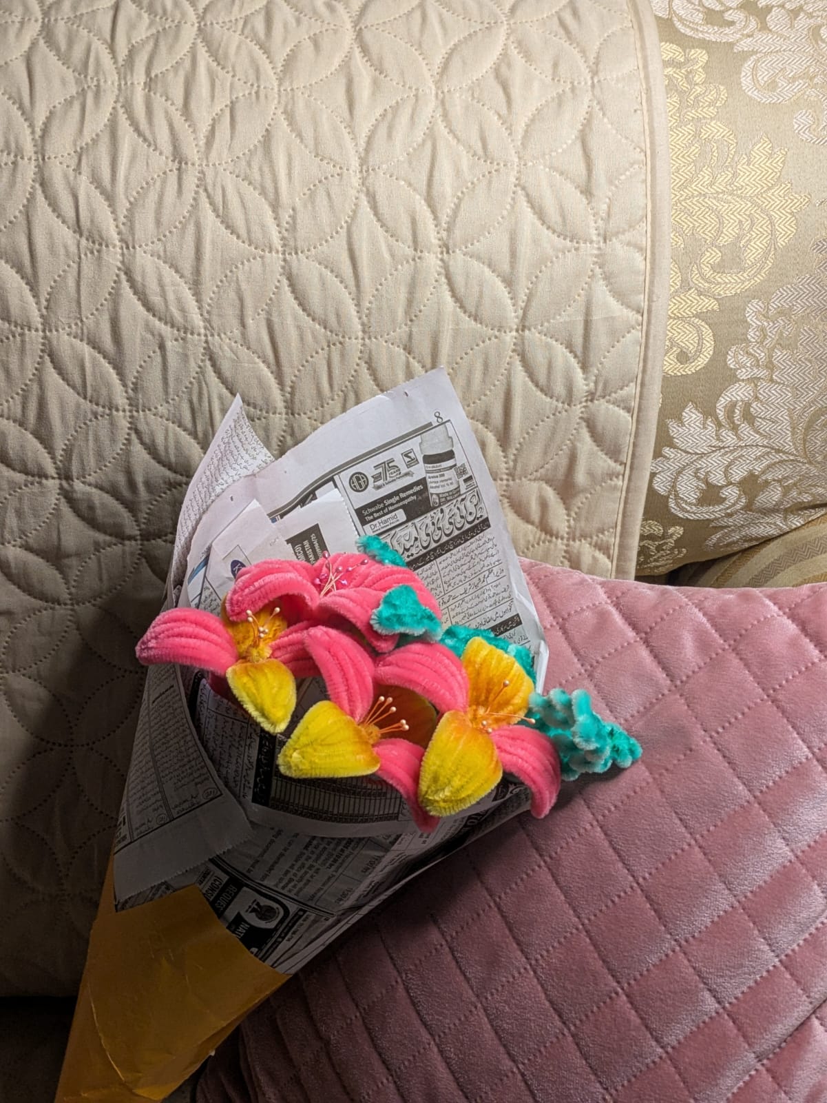 Pink and yellow handmade pipe cleaner flower bouquet wrapped in newspaper, angled composition