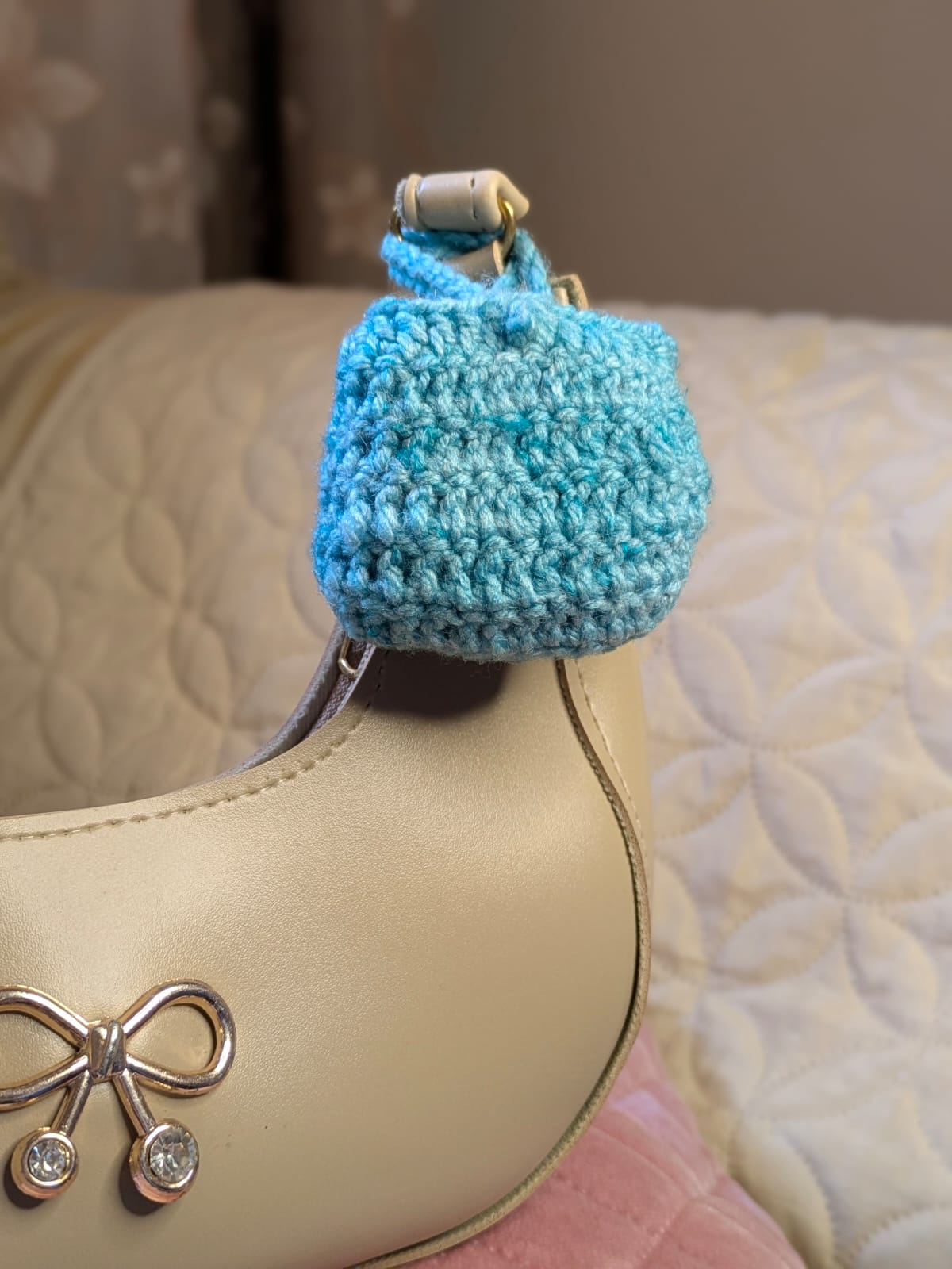 Handmade blue crochet bag charm photographed on a cream leather handbag