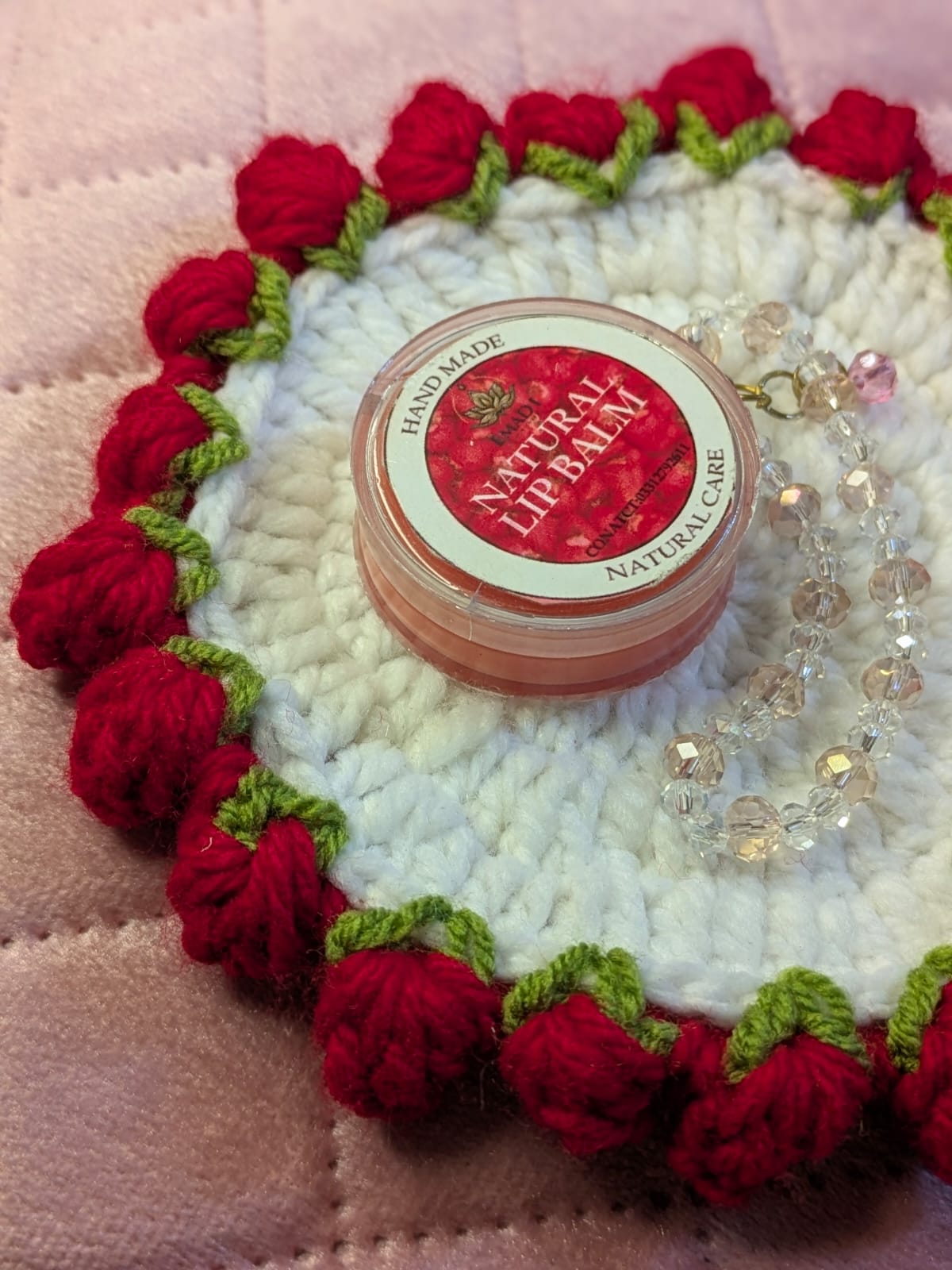 White crochet coaster with red bobble border styled with a natural lip balm and crystal bracelet